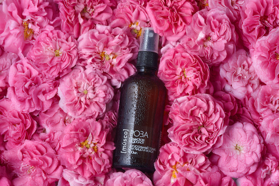Гидролат розы в стеклянном флаконе на фоне свежих цветков роз