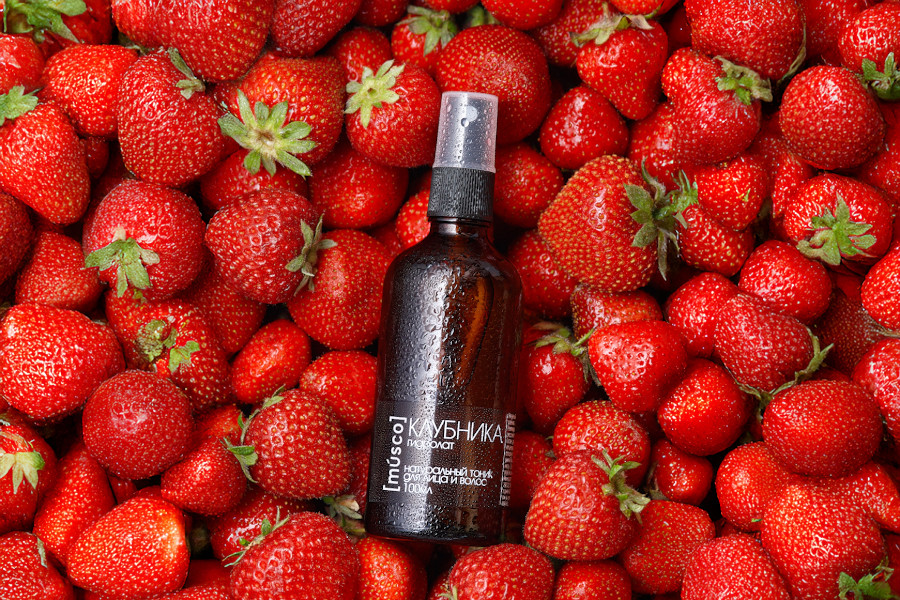 Гидролат клубники в коричневом стеклянном флаконе на фоне свежей сочной клубники