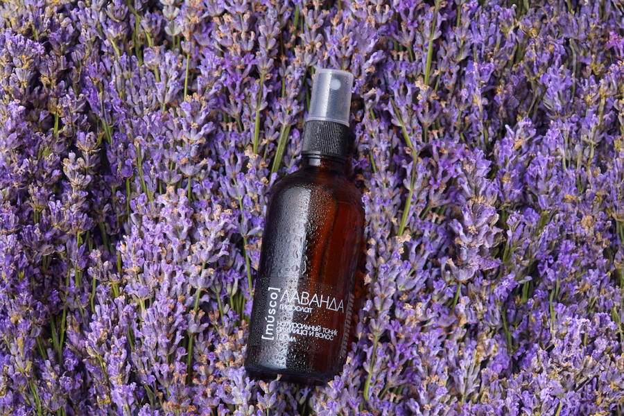 Гидролат лаванды в коричневом стеклянном флаконе на фоне свежих цветков лаванды