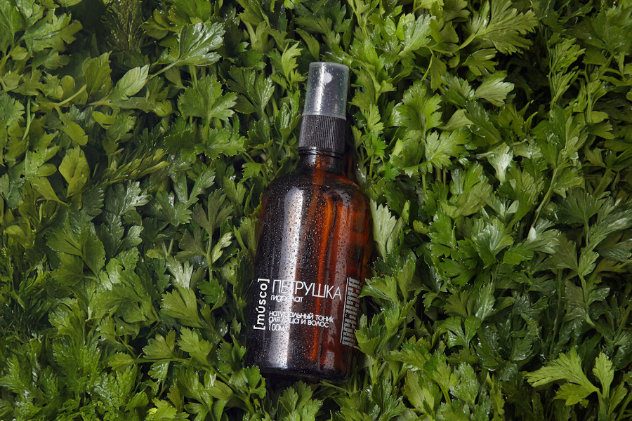 Гидролат петрушки в коричневом стеклянном флаконе на фоне свежих листьев петрушки